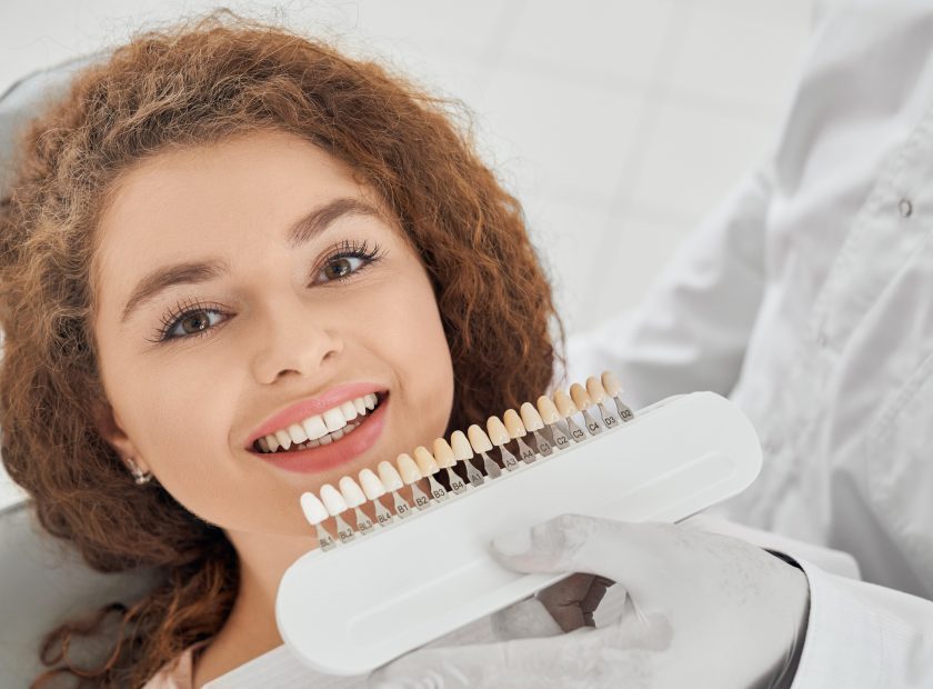 Woman smiling while male dentist keeping teeth color range